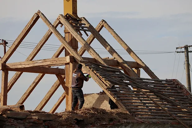 Odkrytý dřevěný krov a dělník při demontáži