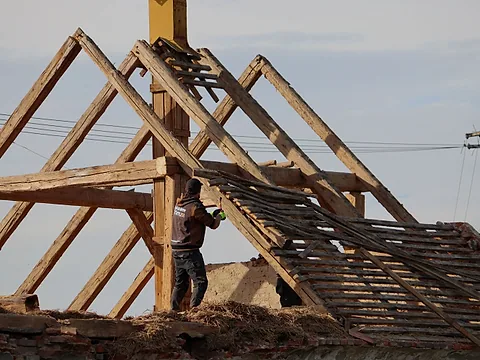 Dělník rozebírá odkrytý dřevěný krov staré stavby