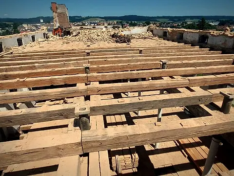 Po: odkryté masivní stropní trámy v řadách, očištěné od suti