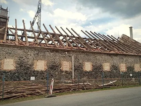 Dlouhá kamenná budova statku se strženou krytinou a odkrytými krokvemi před demolicí